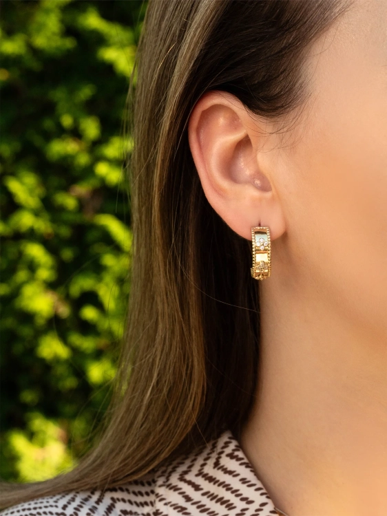 Modne złote kolczyki zdobione lśniącymi cyrkoniami na uchu kobiety