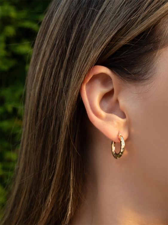 Modne złote kolczyki w kształcie koła z młotkowaną powierzchnią na uchu kobiety