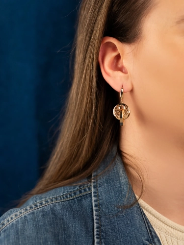 Złote kolczyki 585 widoczne na uchu kobiety, geometryczny splot, wyrazisty połysk, stylowa biżuteria Coomi