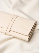 Zbliżenie na detal organizera podróżnego na biżuerię zapinanego na pasek z logo marki Coomi