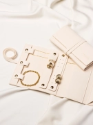 Rozłożony organizer na biżuterię, w środku złota bransoletka, złote pierścionki oraz złote kolczyki, obok drugie zamknięte etui