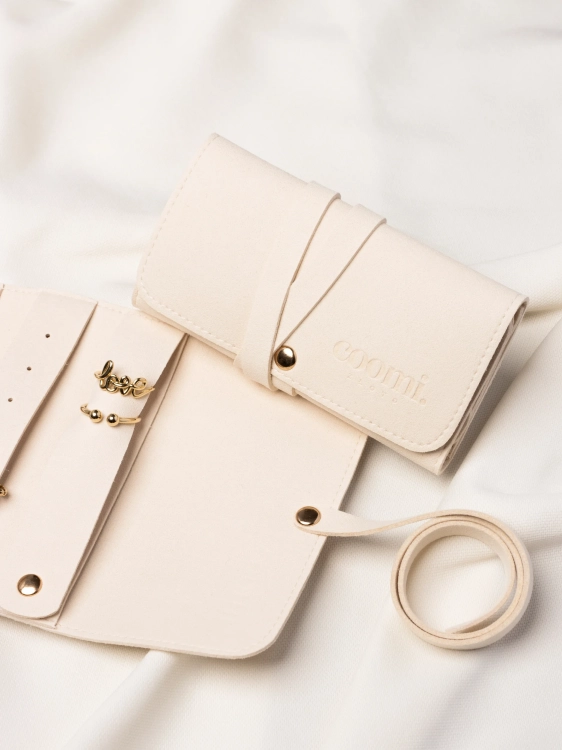 Zbliżenie na detale organizera na złotą biżuterię oraz zamknięte etui z logo Coomi w tle