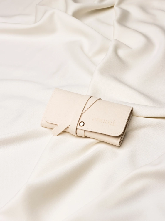 Zwinięte etui podróżne na biżuterię owinięte paskiem zabezpieczającym, na tle jasnej tkaniny